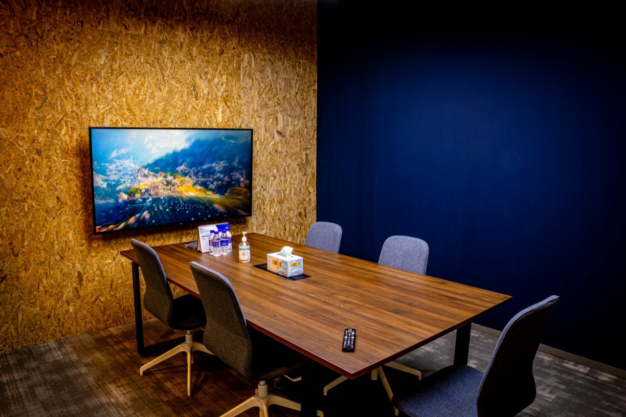 A small meeting room with a wall-mounted display, a wooden table and chairs.
