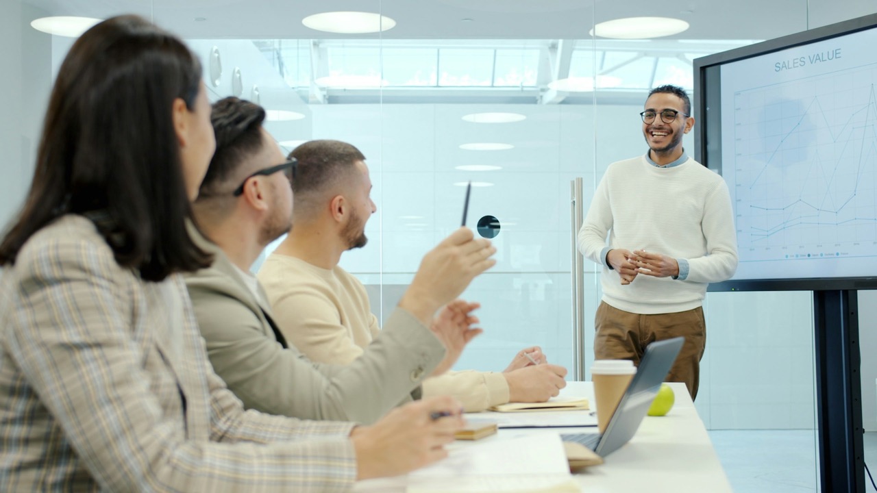 A presenter taking questions from a small team around a meeting table.